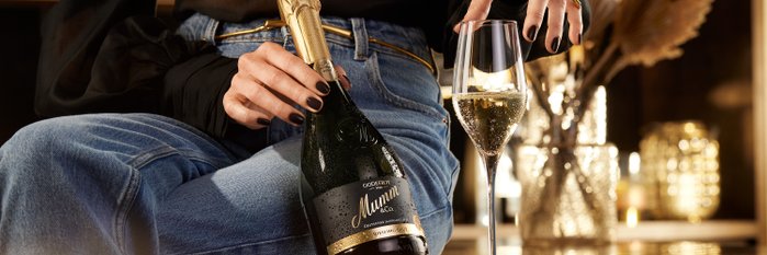 Die Person in Jeans und schwarzem Oberteil genießt einen festlichen Moment mit Sekt und einem glitzernden Glas.