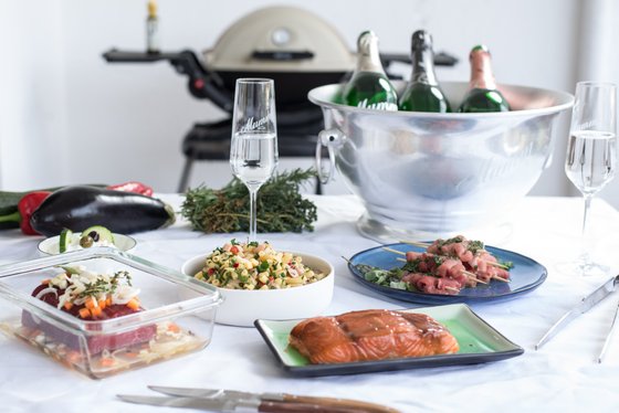 Ein festlich gedeckter Tisch mit verschiedenen Gerichten, darunter Lachs, Pasta-Salat und gegrilltes Fleisch, umgeben von frischen Kräutern.