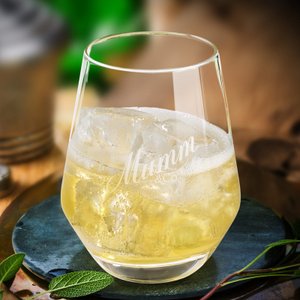 Das Glas mit dem Mumm-Logo enthält ein prickelndes Getränk, umgeben von frischen Kräutern und einer natürlichen Umgebung.