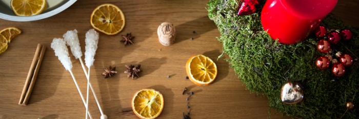 Ein festlich dekorierter Tisch mit einem grünen Kranz, roten Kerzen und getrockneten Orangenscheiben, die eine gemütliche Atmosphäre schaffen.