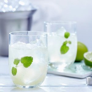 Zwei erfrischende Cocktails mit Eiswürfeln, Minzblättern und Limetten auf einem hellen Tisch, ideal für einen Sommerabend.
