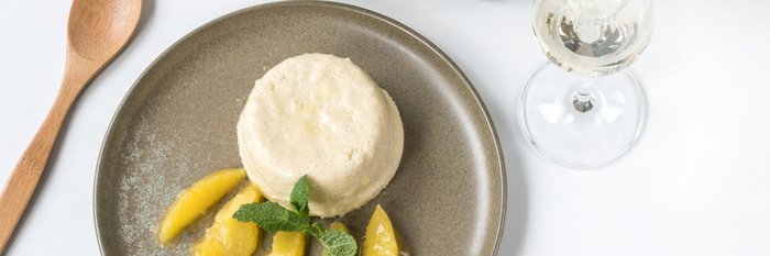 Ein runder Dessertteller mit einer cremigen Nachspeise, umgeben von frischen Mangostücken und einem Minzblatt.