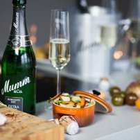 Auf einem eleganten Tisch sind Sekt, ein Glas und eine Schüssel mit frischem Gemüse sowie verschiedene Zutaten zu sehen.