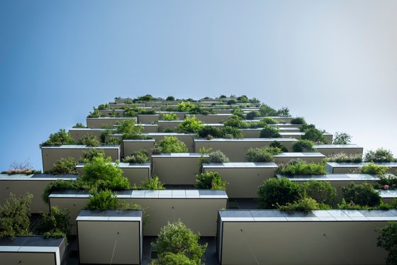Ein modernes Gebäude mit zahlreichen begrünten Balkonen, die üppige Pflanzen und Sträucher zeigen, unter einem klaren blauen Himmel.