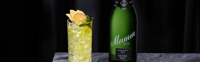 Der erfrischende Drink, dekoriert mit Limettenscheiben und Minze, steht auf einem marmorierten Tisch neben Sekt.