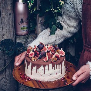 Eine Person hält eine kunstvoll dekorierte Torte mit Feigen, Granatapfelkernen und Walnüssen in einer natürlichen Umgebung.