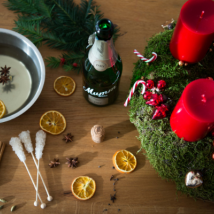 Ein festlicher Adventskranz mit roten Kerzen, umgeben von getrockneten Orangenscheiben und Gewürzen auf einem Holztisch.