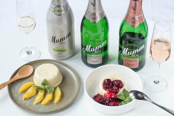 Ein elegantes Arrangement mit alkoholfreiem Sekt, fruchtigem Dessert und frischen Beeren auf einem weißen Tisch.