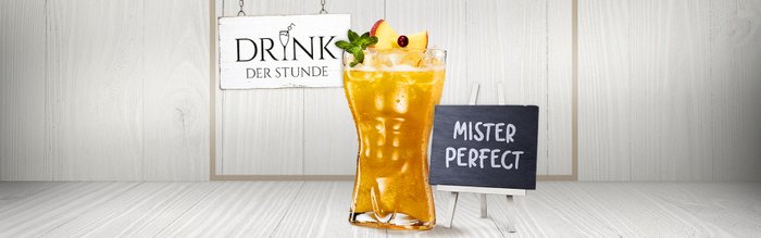 Das Glas mit einem goldenen Cocktail, garniert mit Apfelstücken und Minze, wird von einem kleinen Schild mit 'Mister Perfect' begleitet.