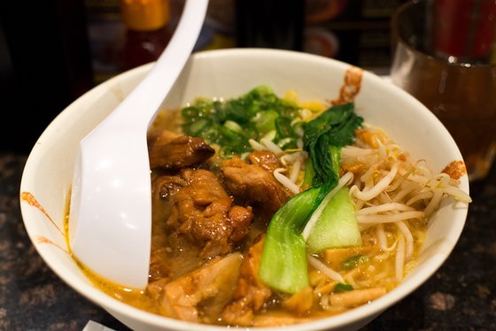 Eine Schüssel mit dampfender Nudelsuppe, gefüllt mit zartem Hähnchen, frischem Gemüse und einer weißen Löffel.