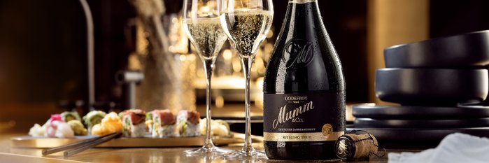 Eine Flasche Godefroy von Mumm Riesling Brut steht neben zwei Gläsern Sekt und einer Auswahl an Sushi auf einem eleganten Tisch.