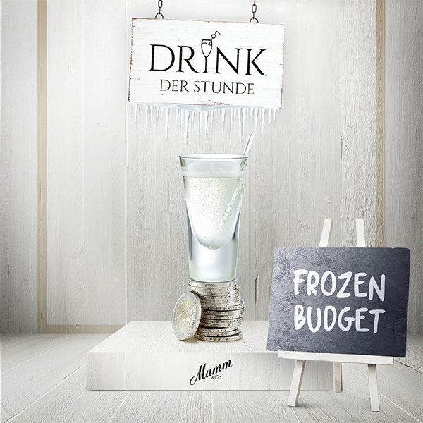 Ein elegantes Glas mit einem klaren Getränk steht auf einem Stapel Münzen, umgeben von einer hellen, minimalistischen Kulisse.