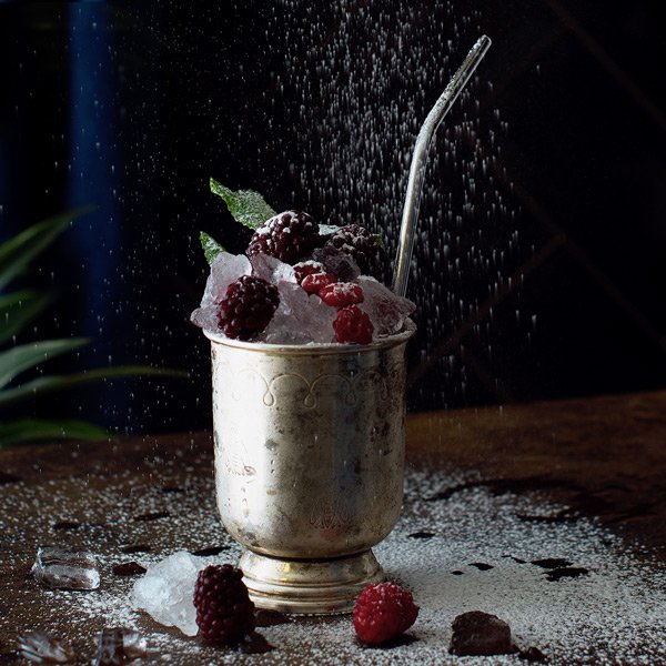Ein silberner Becher gefüllt mit zerstoßenem Eis und frischen Himbeeren, umgeben von einer feinen Zuckerschicht.