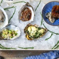 Ein stilvolles Arrangement von Austern auf Eis, mit einer bunten Schale, die eine köstliche Füllung präsentiert, und frischen Kräutern.