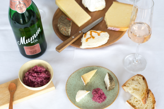 Ein elegantes Arrangement aus verschiedenen Käsesorten, einem Glas Rosé und einem Flasche Sekt auf einem Tisch.