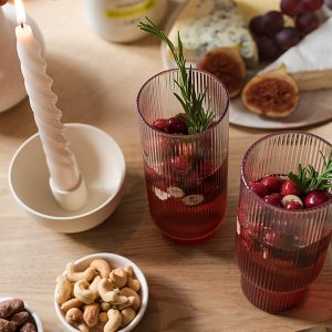 Ein rustikaler Tisch mit zwei dekorativen Gläsern, gefüllt mit Cranberries und frischen Kräutern, sowie einer brennenden Kerze.