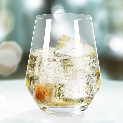 Das Glas enthält ein erfrischendes Getränk mit Eis und einem Zuckerstück, vor einem verschwommenen, leuchtenden Hintergrund.