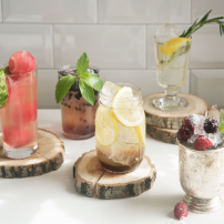 Bunte Getränke in Gläsern, dekoriert mit Minze und Zitrone, präsentieren sich auf rustikalen Holzunterlagen in hellem Licht.