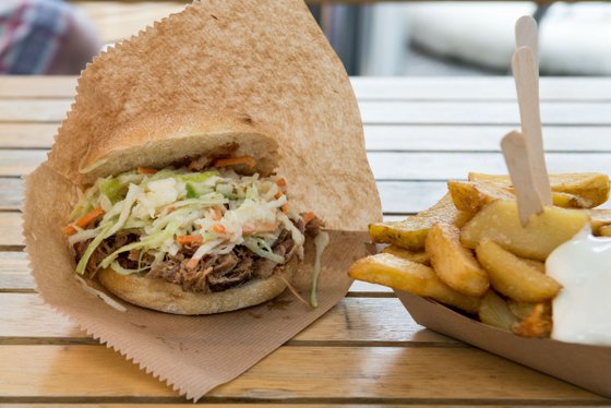 Ein frisch zubereiteter Sandwich mit zartem Fleisch und knackigem Krautsalat, serviert auf einem braunen Papier.