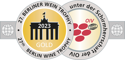 Ein stilisiertes Abzeichen mit dem Brandenburger Tor, das die Goldmedaille der Berliner Wein Trophy 2023 darstellt, umrahmt von Weintrauben.