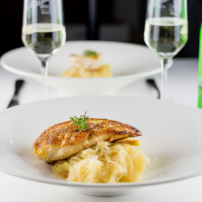 Ein elegantes Gericht mit gebratenem Hähnchenfilet auf einem Bett aus Kartoffelpüree, umgeben von zwei Gläsern Sekt.
