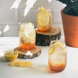 Drei Gläser mit Eistee stehen auf Holzscheiben, dekoriert mit Zitronenscheiben und umgeben von frischen Zitronen.