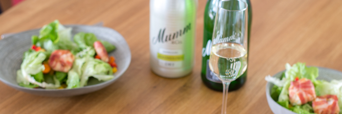 Auf einem Tisch liegen zwei Schalen mit buntem Salat, während ein Glas Sekt und zwei Flaschen im Hintergrund stehen.