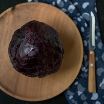 Ein lila Kohlkopf auf einem Holzbrett, umgeben von einem blauen Tuch, das mit weißen Punkten dekoriert ist.