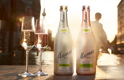 Zwei Flaschen alkoholfreier Sekt stehen neben zwei Gläsern, während die Sonne im Hintergrund untergeht.