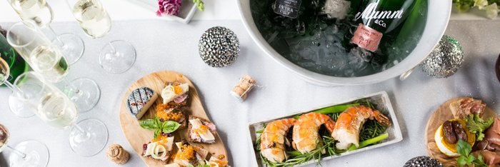 Ein eleganter Tisch mit verschiedenen Delikatessen, darunter Meeresfrüchte, Käse und frische Kräuter, umgeben von Gläsern Sekt.
