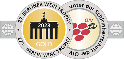 Ein stilisiertes Abzeichen mit dem Brandenburger Tor, das die Goldmedaille der Berliner Wein Trophy 2023 darstellt, umrahmt von Weintrauben.
