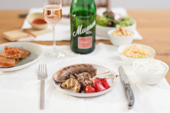 Ein gedeckter Tisch mit einer Auswahl an köstlichen Speisen, darunter gegrillte Würstchen und frisches Gemüse.