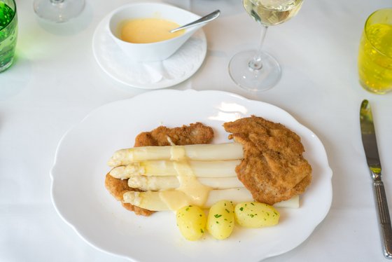 Ein Teller mit zartem, weißem Spargel, umgeben von knusprigem Schnitzel und kleinen, gekochten Kartoffeln.