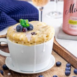 Eine Tasse mit einem köstlichen, überlaufenden Kuchen, garniert mit frischen Heidelbeeren und einem Minzblatt.