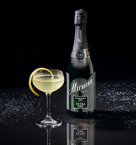 Eine Flasche Mumm Sekt steht neben einem eleganten Cocktailglas mit einem Zitronenzesten, auf einem glänzenden Tisch.