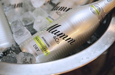 Eine silberne Flasche Mumm Sekt steht in einem Eiskübel, umgeben von Eiswürfeln und zerstoßenem Eis.