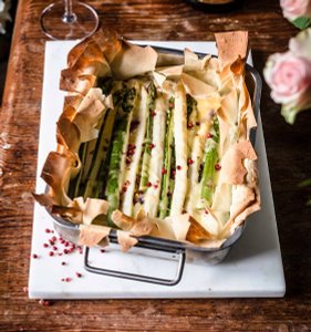 Ein rechteckiger Auflauf mit grünem Spargel, umhüllt von knusprigem Teig und garniert mit rosa Pfefferkörnern.