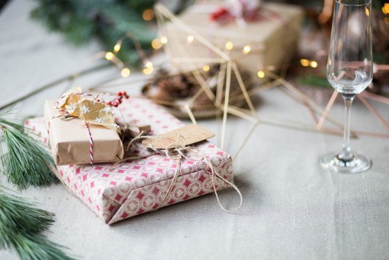 Ein hübsch verpacktes Geschenk mit einer Schnur und einer kleinen Karte steht neben einem Glas, umgeben von Weihnachtsdekoration.
