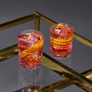 Ein elegantes Arrangement von zwei Cocktails in Kristallgläsern, gefüllt mit Eis und frischen Orangenscheiben auf einem Tisch.