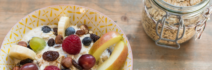 Eine Schüssel mit Joghurt, frischen Früchten und Nüssen, umgeben von einem rustikalen Holztisch und einem Glas Haferflocken.