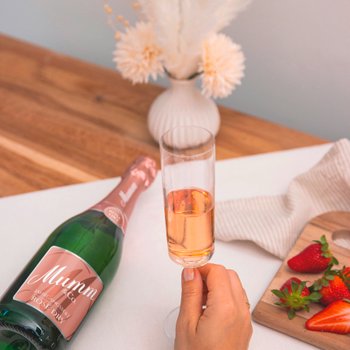 Ein Glas mit roséfarbenem Sekt wird von einer Hand gehalten, während eine Flasche Mumm daneben steht.