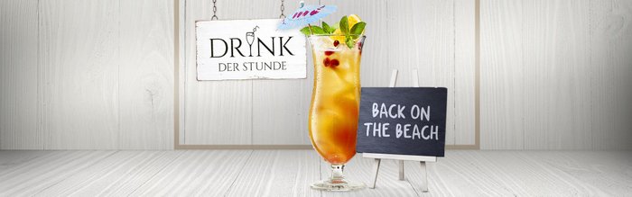 Auf einem Tisch steht ein bunter Drink mit Früchten und Minze, daneben ein Schild mit der Aufschrift 'BACK ON THE BEACH'.