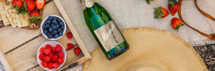 Ein Picknick-Setup mit Sekt, frischen Früchten und Crackern, umgeben von einer natürlichen Umgebung und einer gemütlichen Decke.