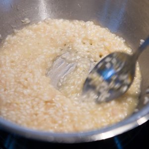 Der Topf enthält eine schaumige Risotto-Mischung, die mit einem glänzenden Löffel umgerührt wird, bereit zum Servieren.