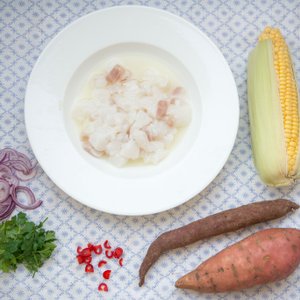 Ein Teller mit frischem Fisch in einer klaren Brühe, umgeben von buntem Gemüse wie Süßkartoffeln und Maiskolben.