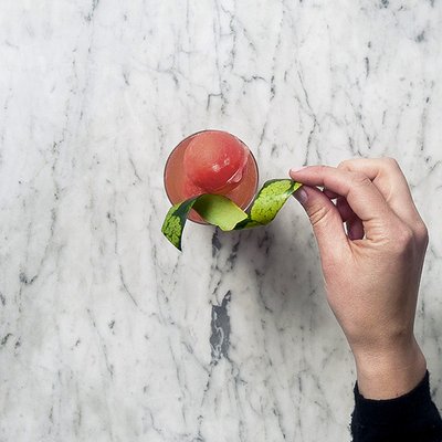 Auf einem marmorierten Tisch liegt ein Glas mit rotem Sorbet, während eine Hand eine Limettenschale anhebt.