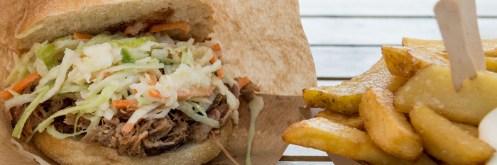 Das Bild zeigt einen Döner mit Fleisch und Krautsalat, zusammen mit einer Portion knuspriger Kartoffelspalten in der Nähe.