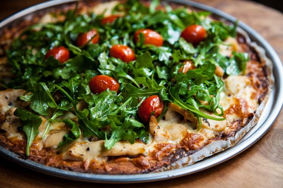 Eine frisch gebackene Pizza mit knusprigem Rand, belegt mit Rucola und saftigen Kirschtomaten, auf einem Holzuntergrund.