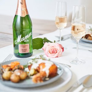 Ein eleganter Tisch gedeckt mit köstlichem Essen, einer Flasche Mumm Sekt und einer zarten rosa Rose als Dekoration.