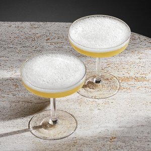 Auf einem hellen Tisch sind zwei Gläser mit schaumigen, gelben Cocktails platziert, die einladend und frisch wirken.
